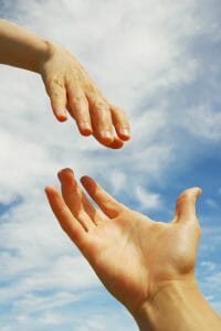 one hand reaching down to another in front of a blue sky. Lending a helping hand.