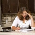 stressed woman looking at bills while sitting in the kitchen needs divorce financial planning