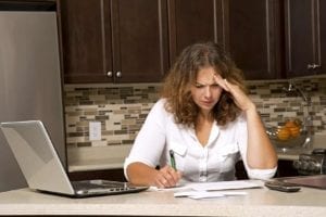 stressed woman looking at bills while sitting in the kitchen needs divorce financial planning