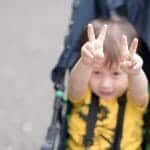 Child in stroller holding up peace signs with both hands, signifying peaceful divorce