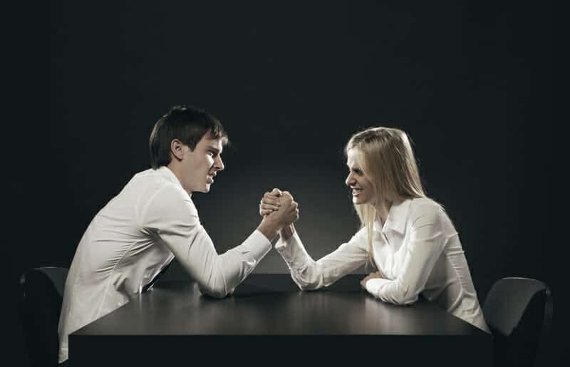 Man and woman in a contested divorce arm wrestling at a table.