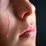 Close up of a woman with a tear running down her cheek as she is wondering how to deal with heartbreak