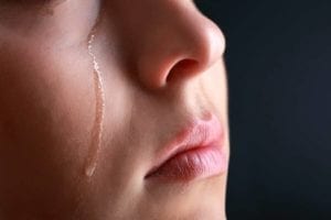 Close up of a woman with a tear running down her cheek as she is wondering how to deal with heartbreak