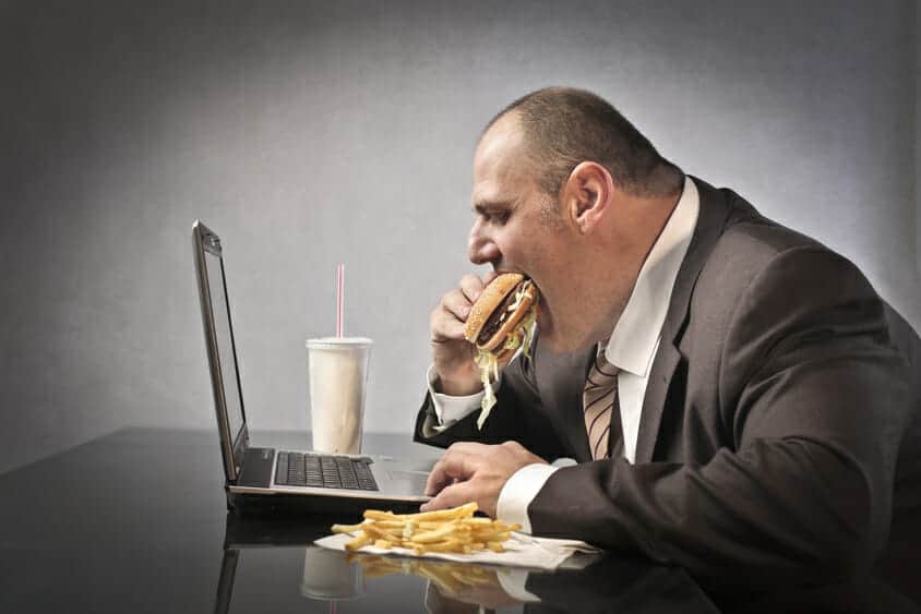 Fat business man working at a laptop while gorging on a hamburger and fries