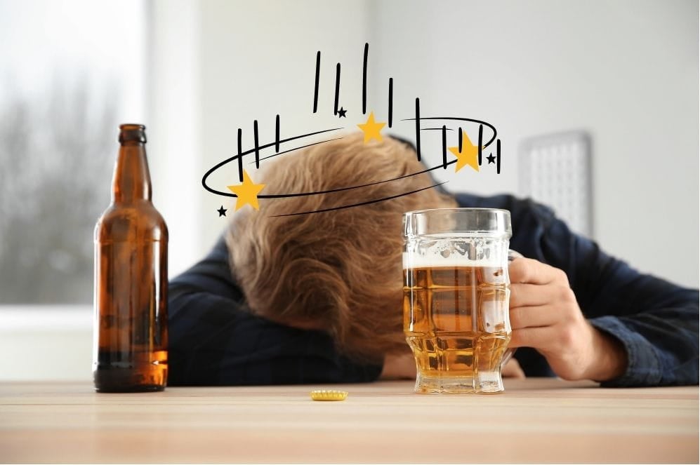 A man passed out drunk on a table, with a bottle of alcohol