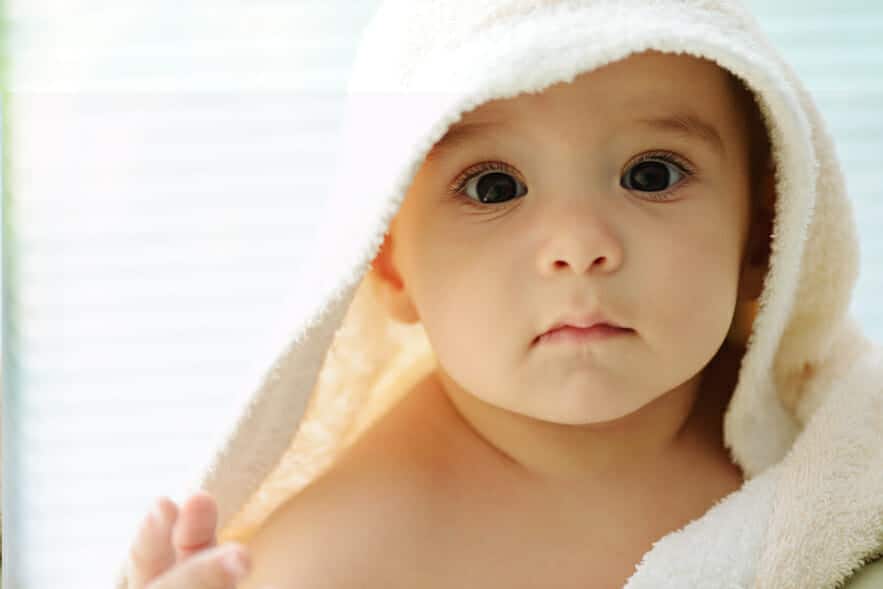 Portrait of angelic baby looking out from under a white towel.