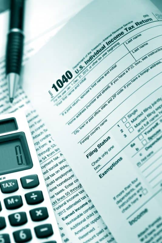 Close up of 1040 Tax Returns with a calculator and pen on top.