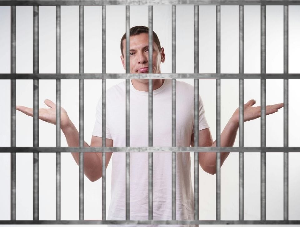 An adult man behind bars, shrugging