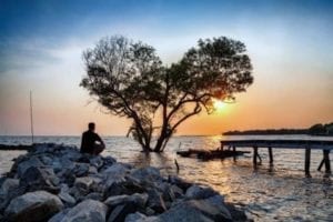 Man dealing with his emotions sitting on rocks by a lake at sunset