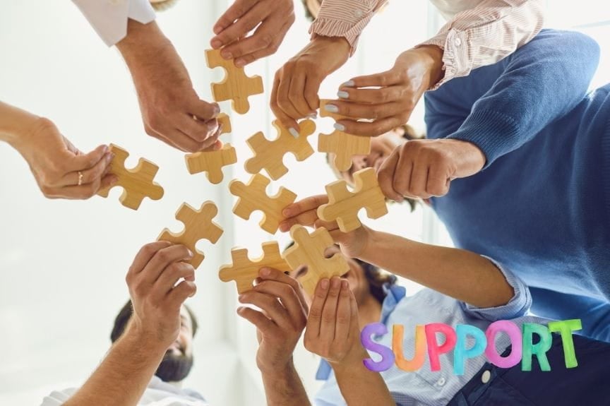 Several hands reaching towards the center, each holding a puzzle piece symbolizing support