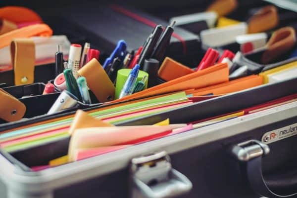 Container with file folders, post its and pencils.