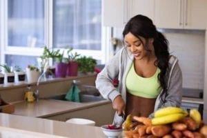 Pretty woman in workout gear chopping fruit in kitchen