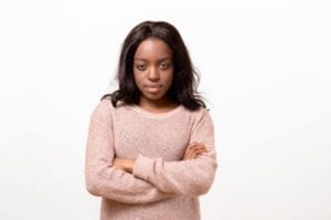 Serious young African American woman standing with folded arms staring at the camera with a calm emotionless expression isolated on white