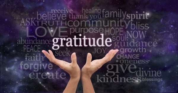 Hands opening to a word cloud of gratitude on a starry purple background