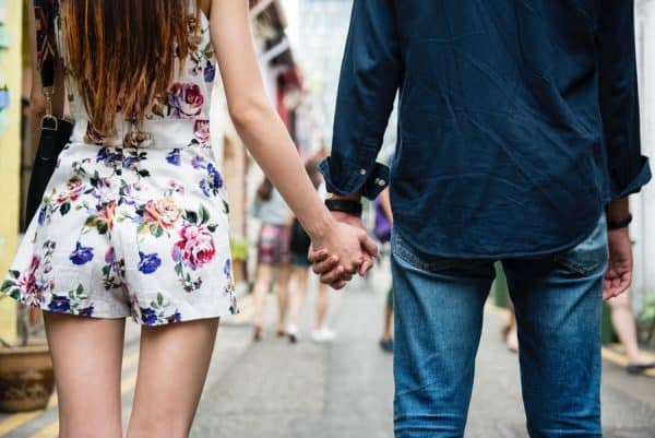 Young woman and man holding hands walking down a city street