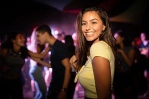 Woman at a divorce party smiling at the camera while the crowd dances behind her.