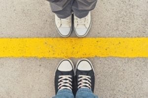 Close up of two people in sneakers standing toe to toe on opposite sides of a yellow line. Signifies mediation strategies.