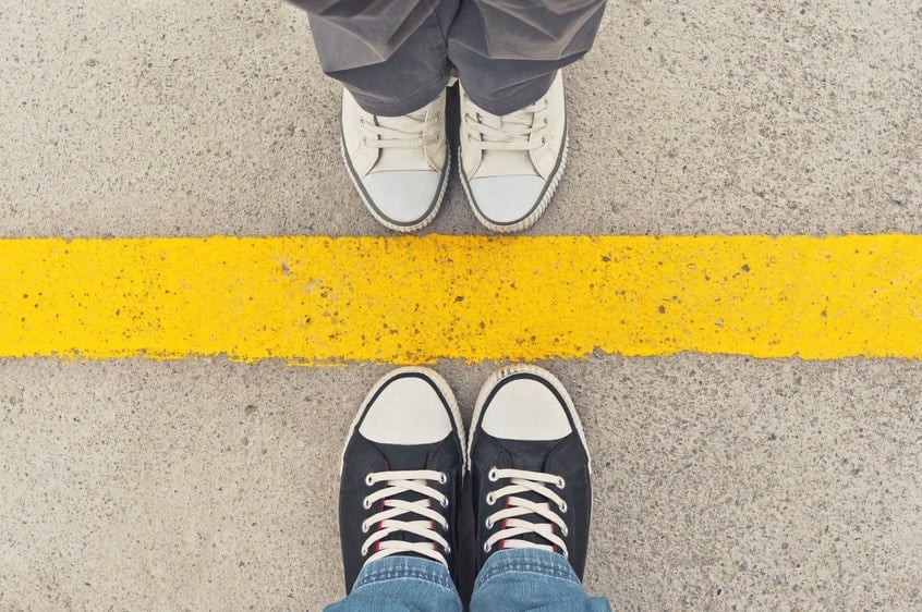 Close up of feet in sneakers standing toe to toe on opposite sides of a yellow line. Signifies mediation strategies.