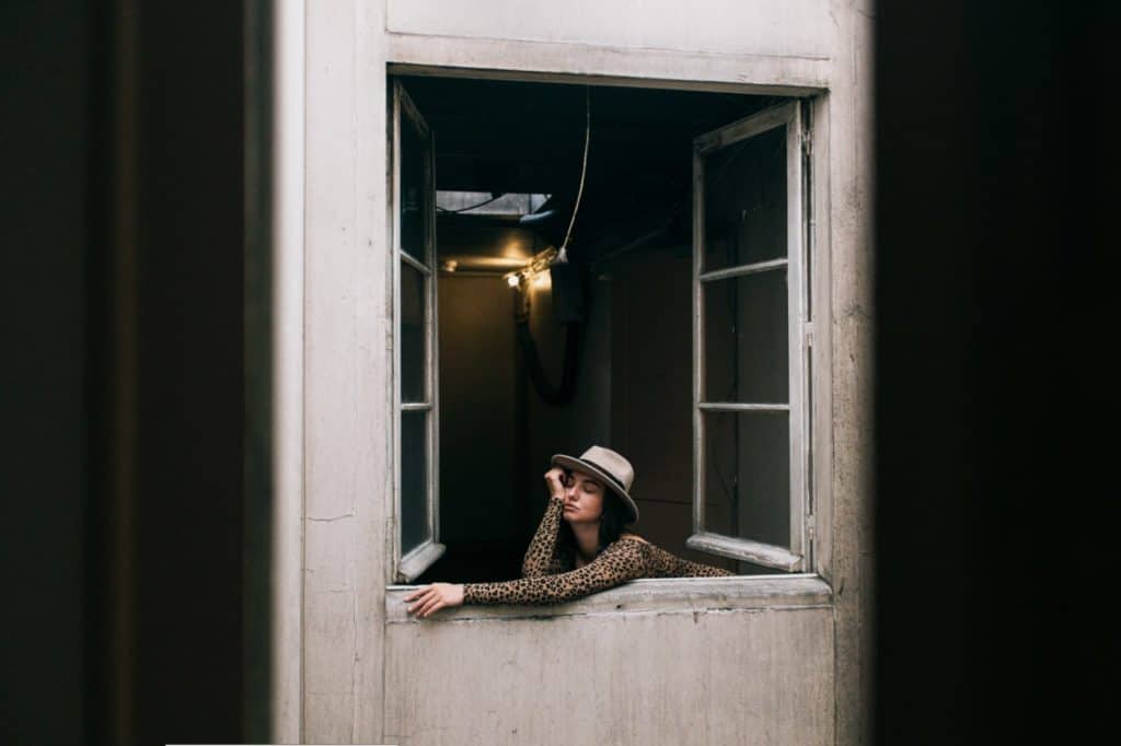 Bored woman looking out an open apartment window trying to escape her marriage during quarantine.