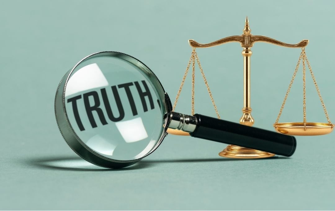 a magnifying glass that says "truth" with the scales of justice behind it