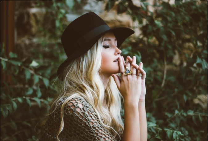 Beautiful young blonde woman in a cowboy hat in a forest clasping her hands in prayer