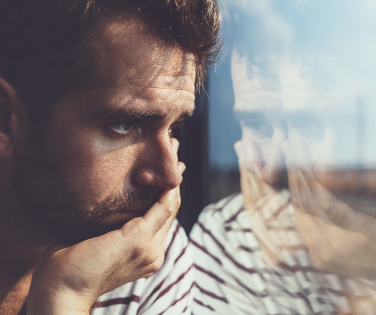 Man contemplating divorce looking out the window with sad reflection.