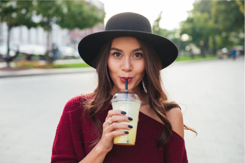 Pretty brunette woman in a hat drinking Kool-Aid from a plastic cup through a straw