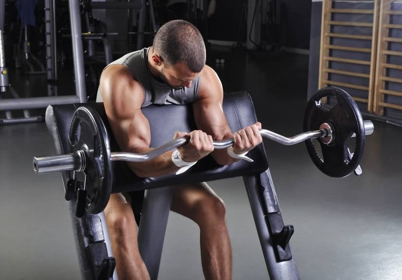 Exercies - Man in a gym doing a bicep curl with a weighted bar.