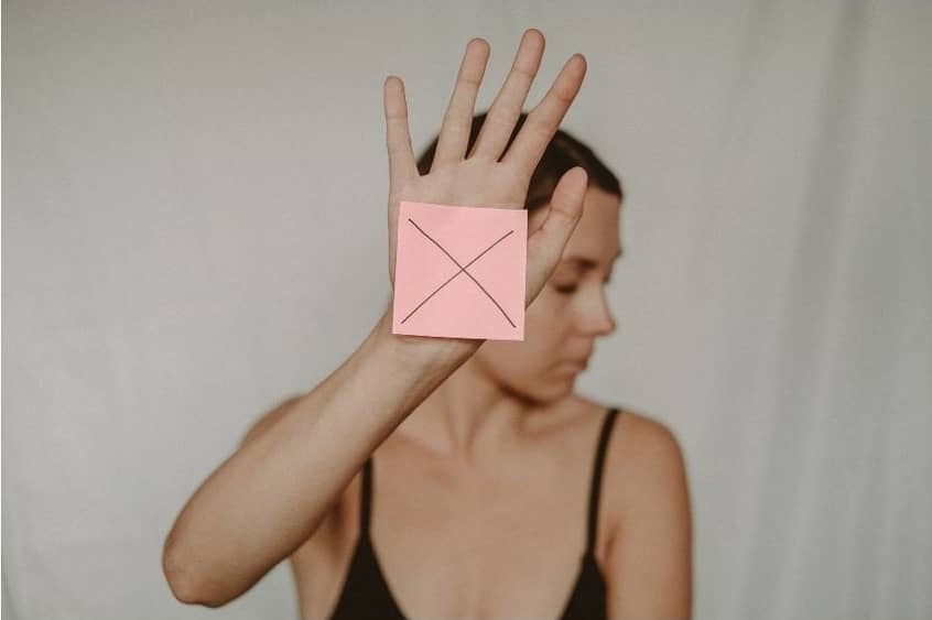 Woman at the limit of her emotional capacity holding her hand up with a post it note with an "X" on it.