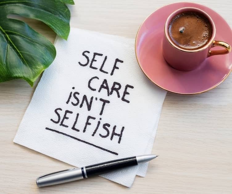 Note on a napkin next to a cup of coffee. "Self care isn't selfish."