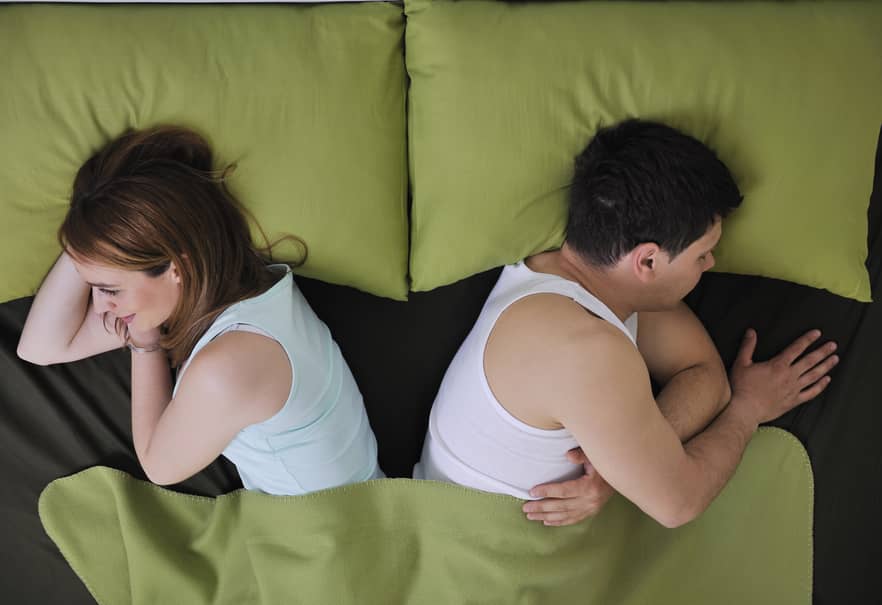 Young couple in bed with their backs to each other, deciding to divorce.