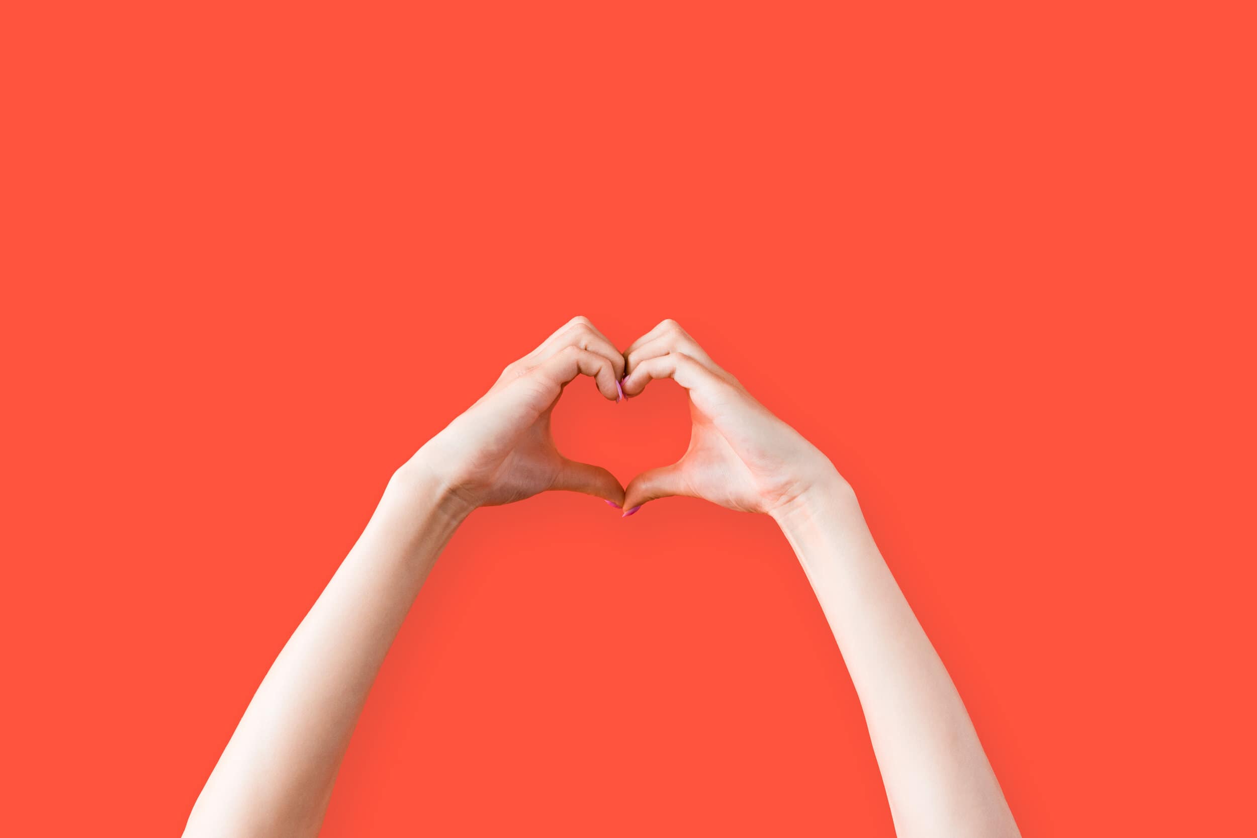 Female hands making a heart in front of a red background - open to love.