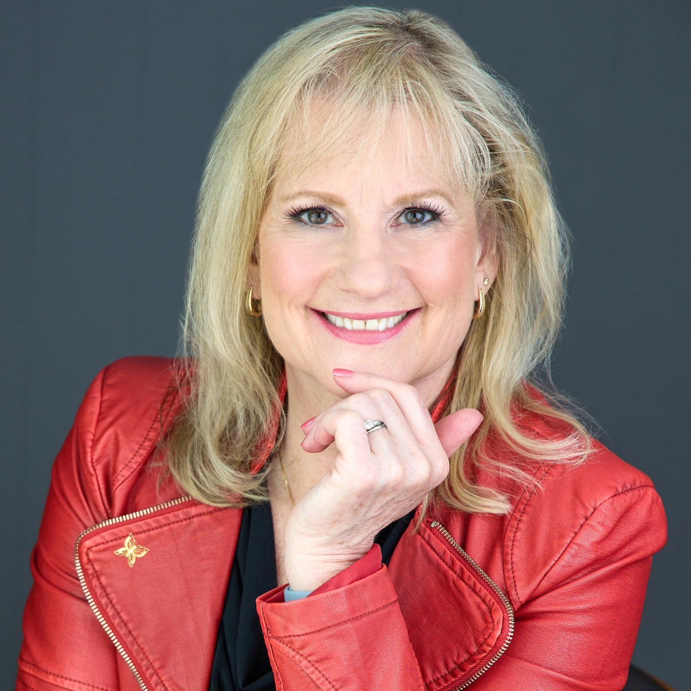 Head shot of Karen Covy in an Orange jacket smiling at the camera with her hand on her chin.