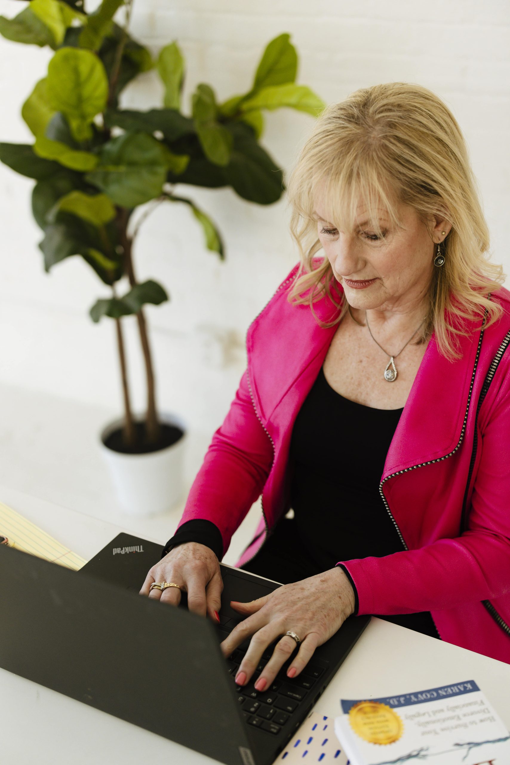 Karen Covy in a pink suit working on a laptop.
