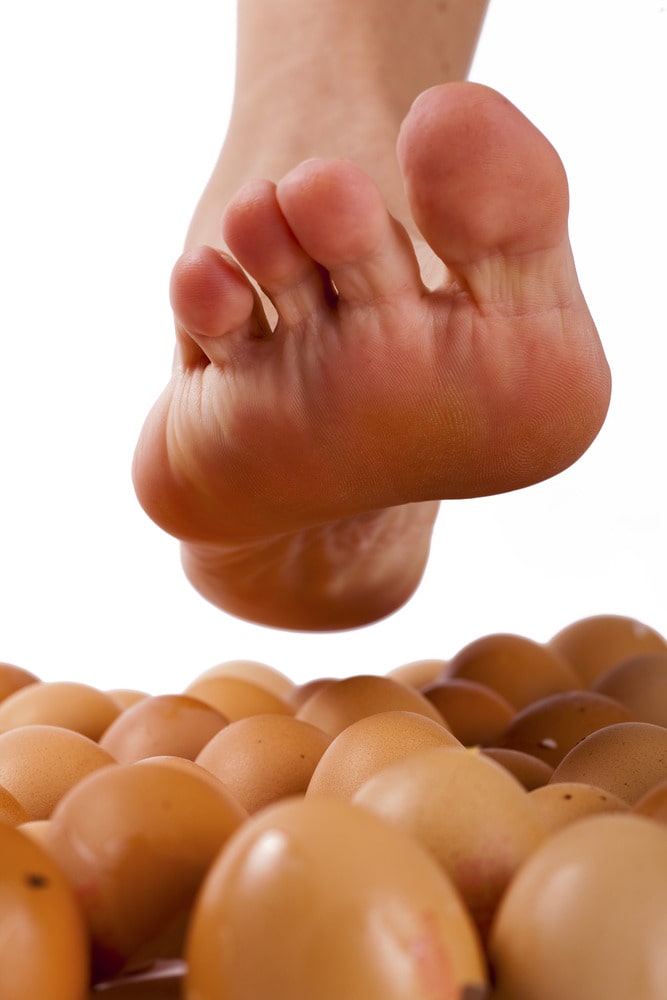Close up of bare foot hovering over brown eggs. Walking on eggshells.