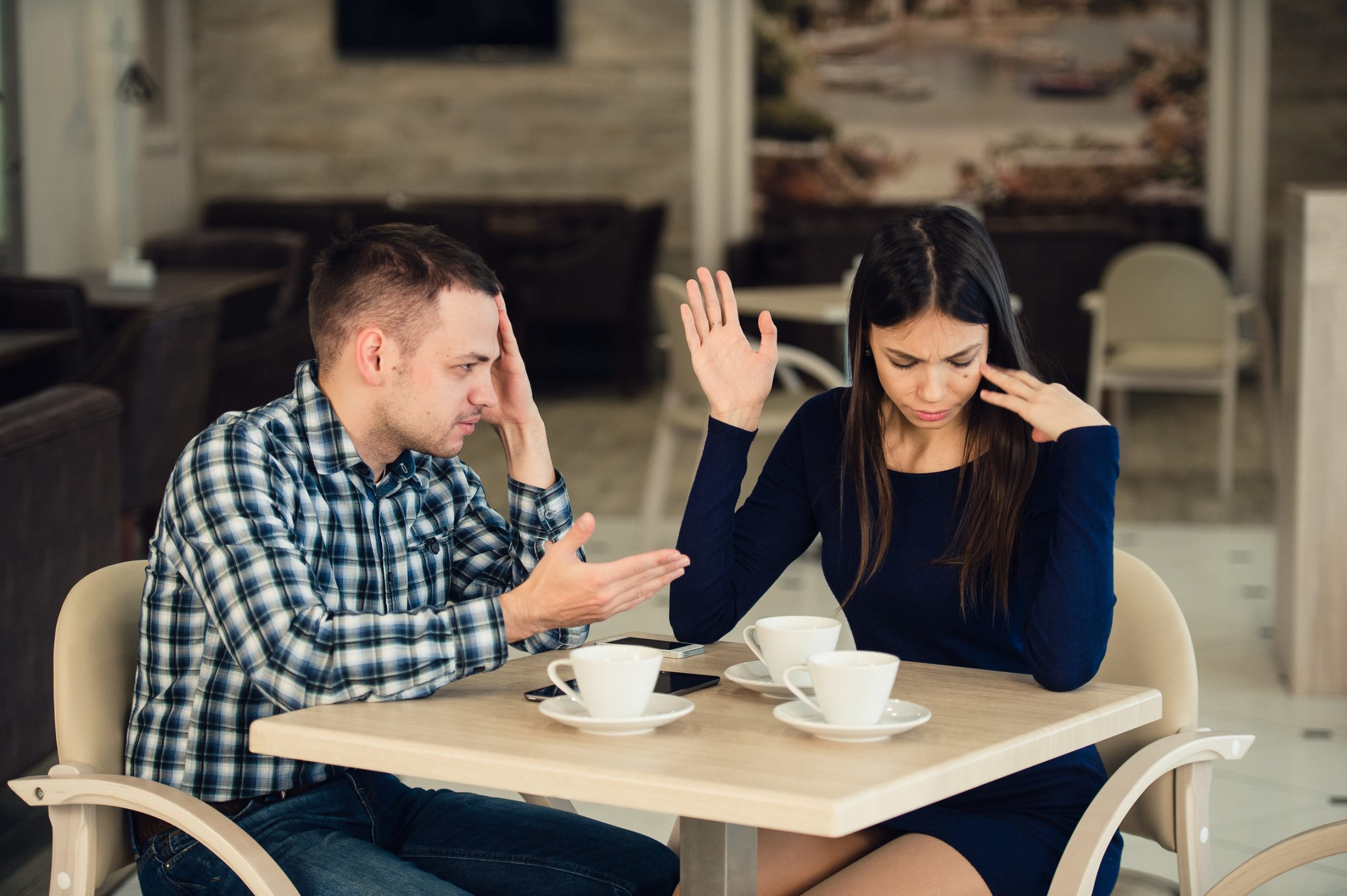 Man and woman in a coffee shop having a difficult conversation. They're not talking, they're both looking away.