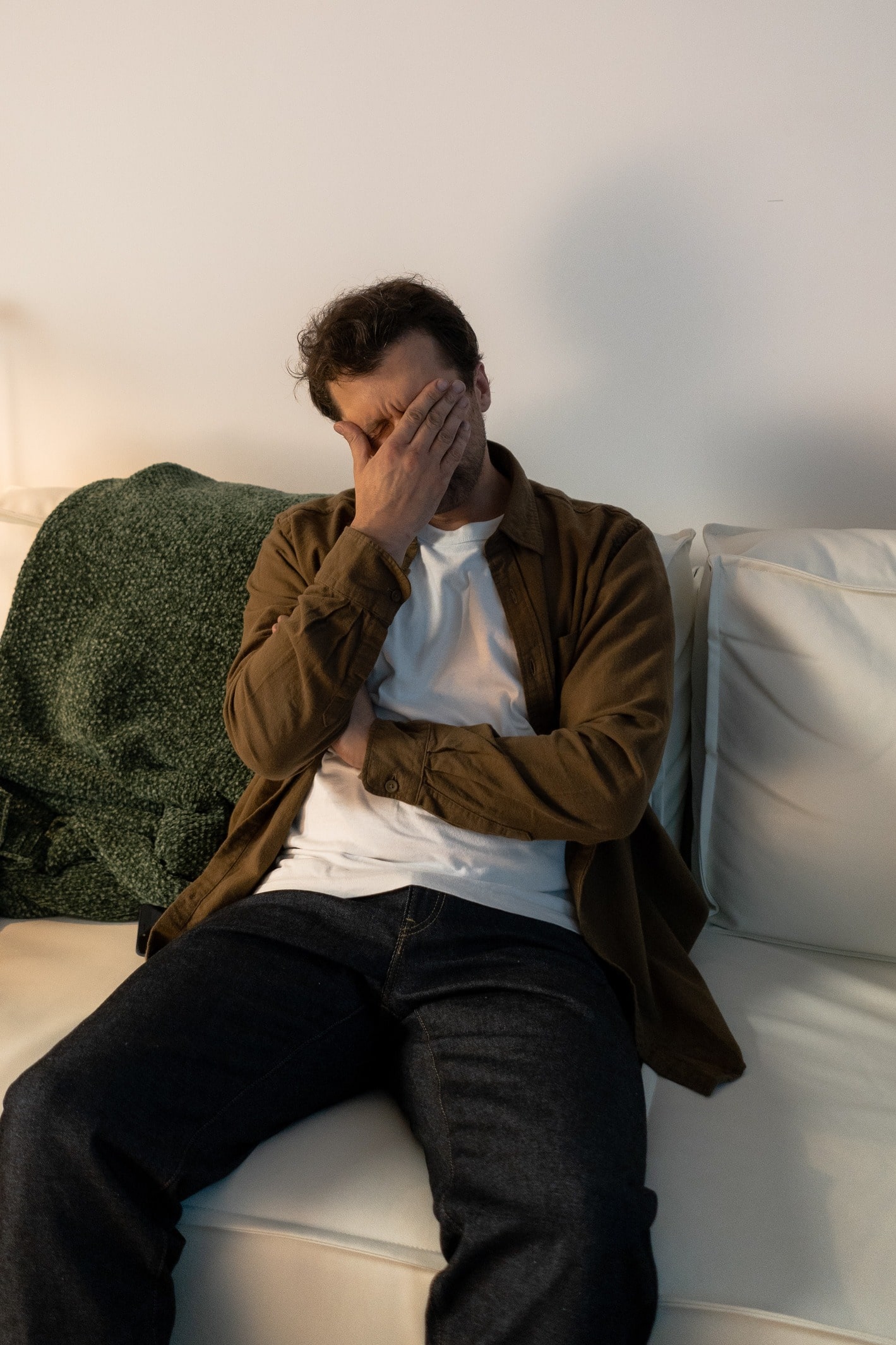 Man with anxiety about money sitting on a couch with his head in his hands.