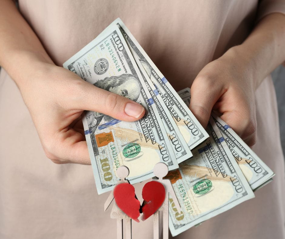 Alimony Hands of a woman counting hundreds of dollars in alimony with a cutout image of a couple with a broken heart on it.