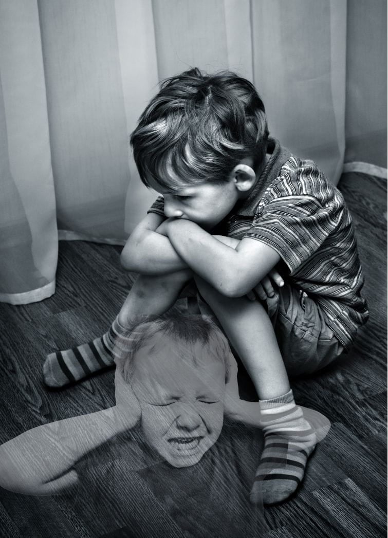A young boy sitting on the floor looking sad and neglected. Another translucent image of a boy putting his hands over his ears is superimposed