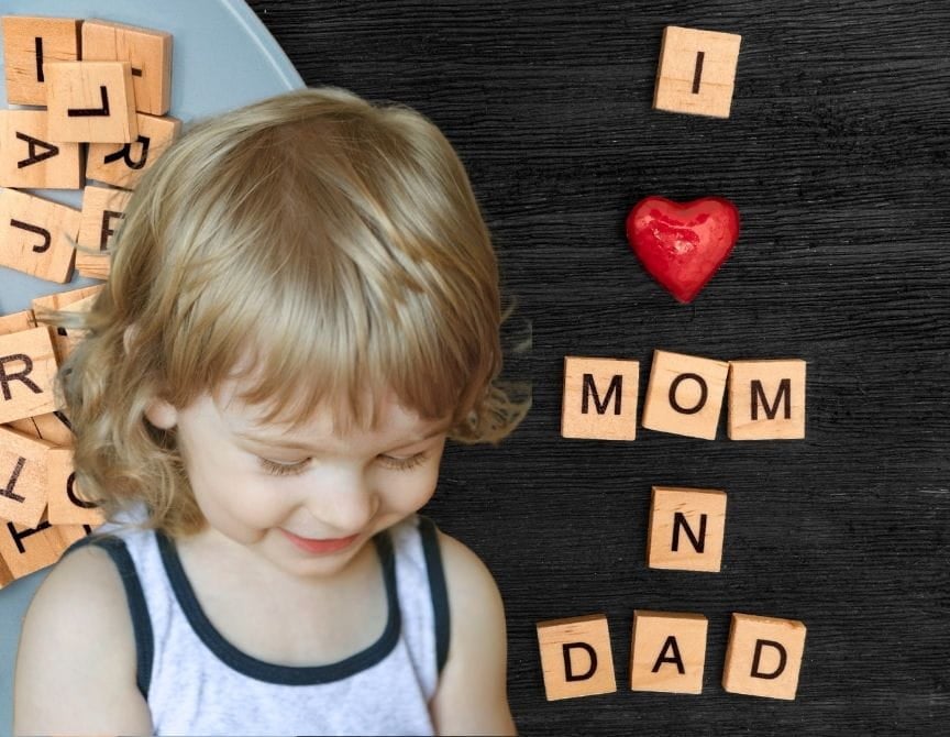 A young girl smiling softly and blocks beside her spelling out "I love mom and dad"