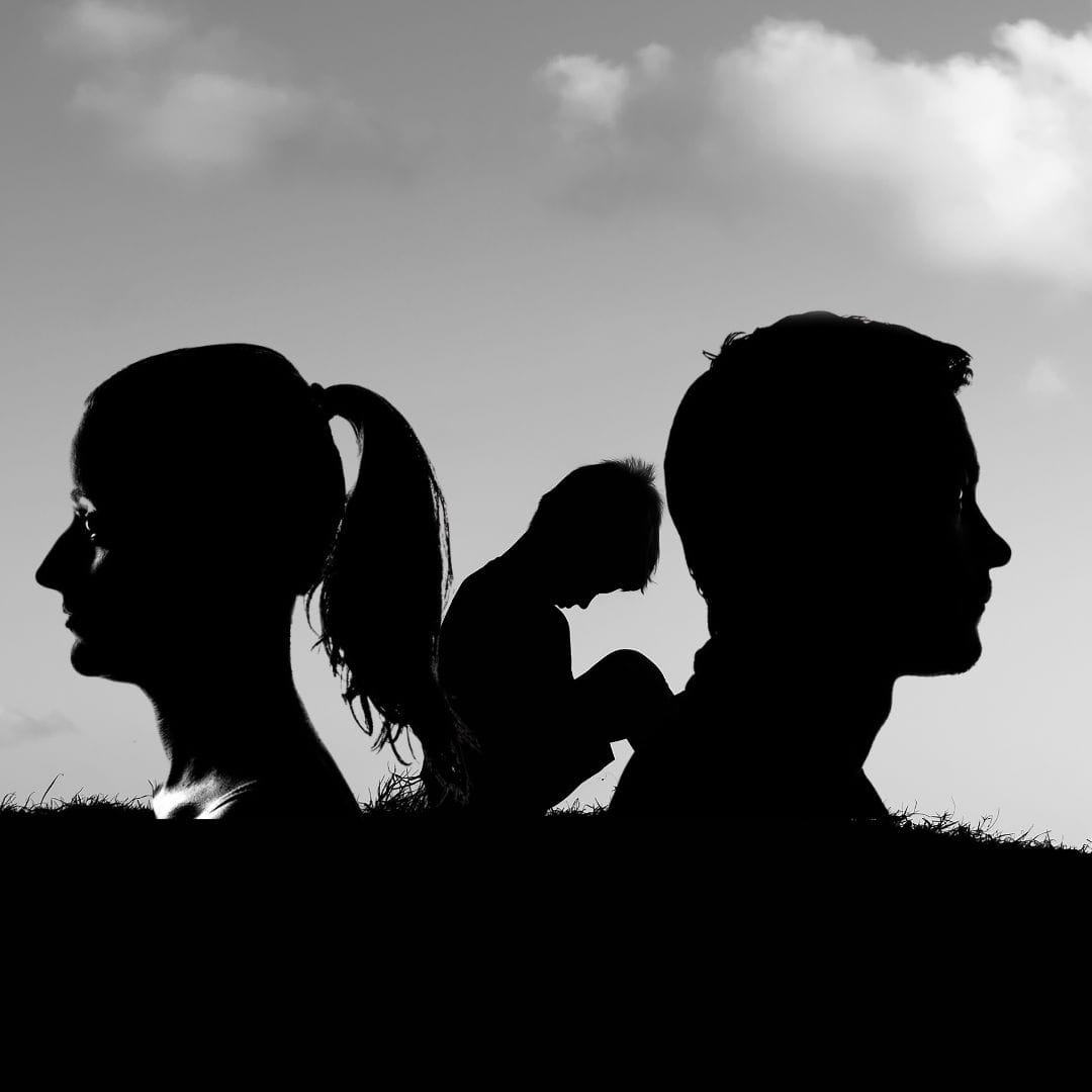 Silhouette of an upset child between silhouette of man and woman facing away from each other. Child of divorce.