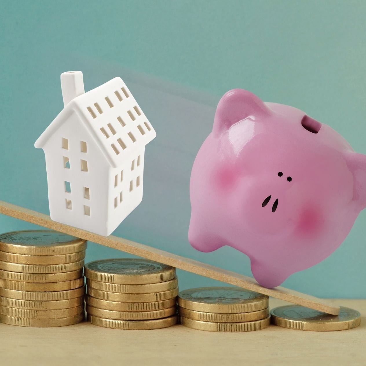 House tipping a piggy bank on a see-saw over money.