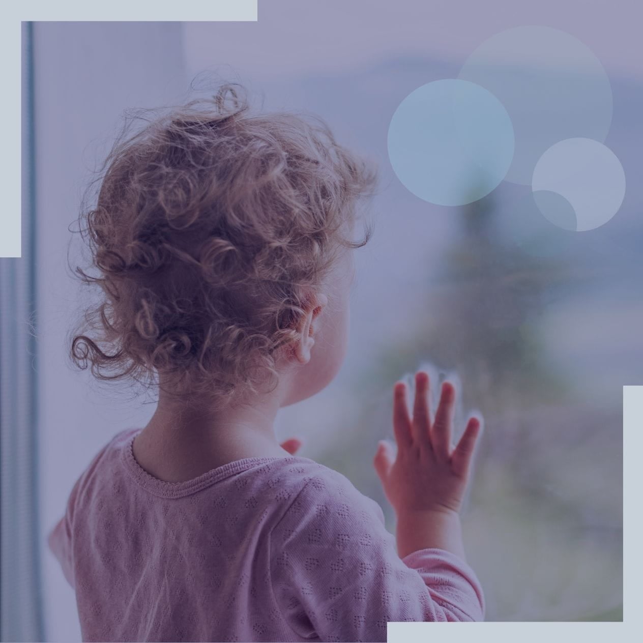 Wistful small lonely child looking out the window on a blue day.