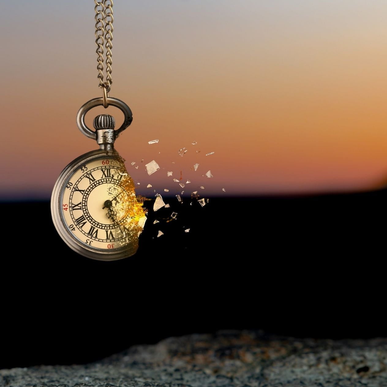 Pocket watch breaking apart in front of sunset background.